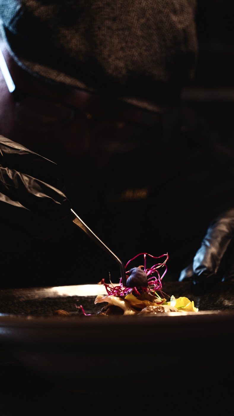 Chef qui dresse une assiette avec une pince, dans la pénombre