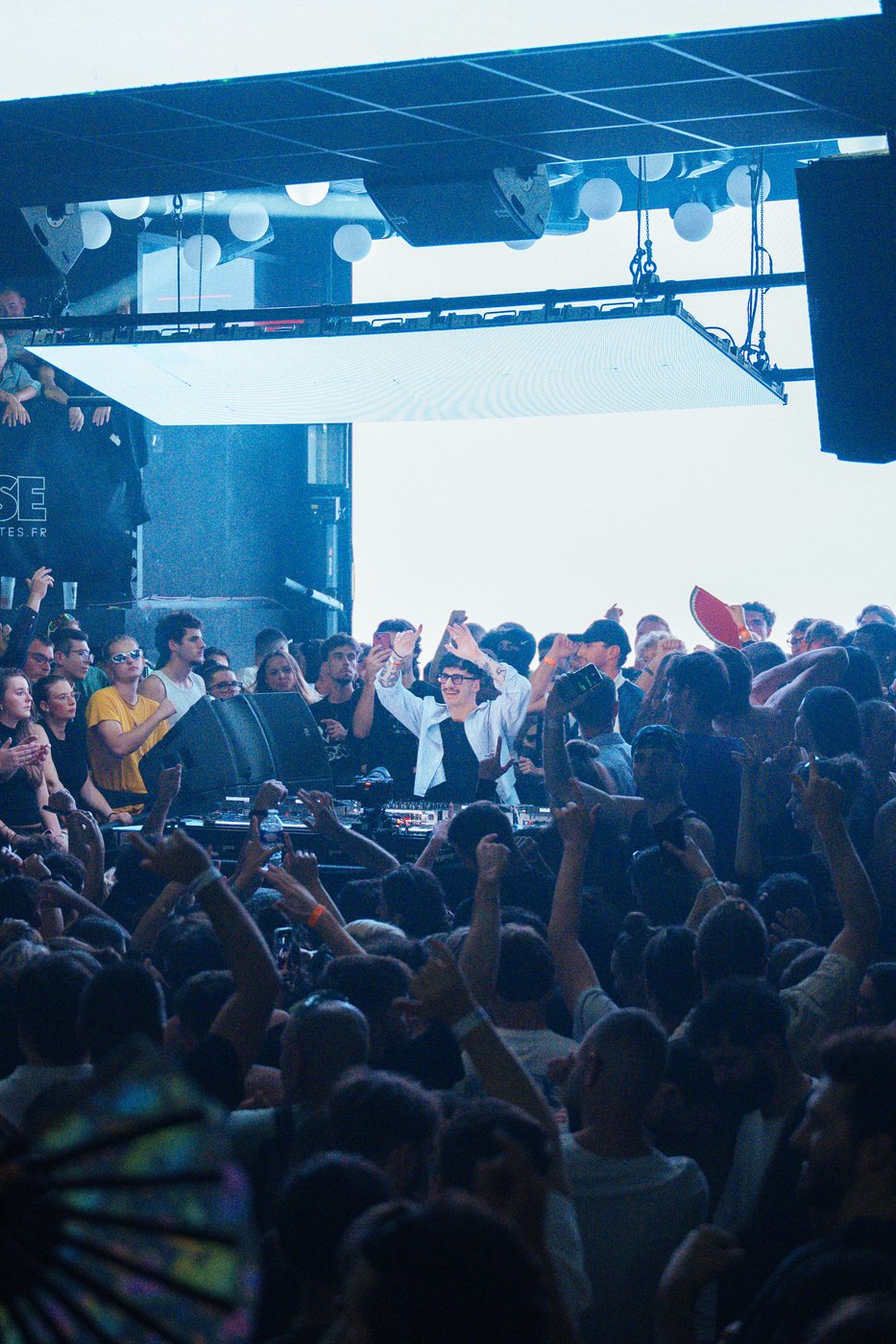 DJ les bras levés au milieu d'une foule en soirée, dans un club