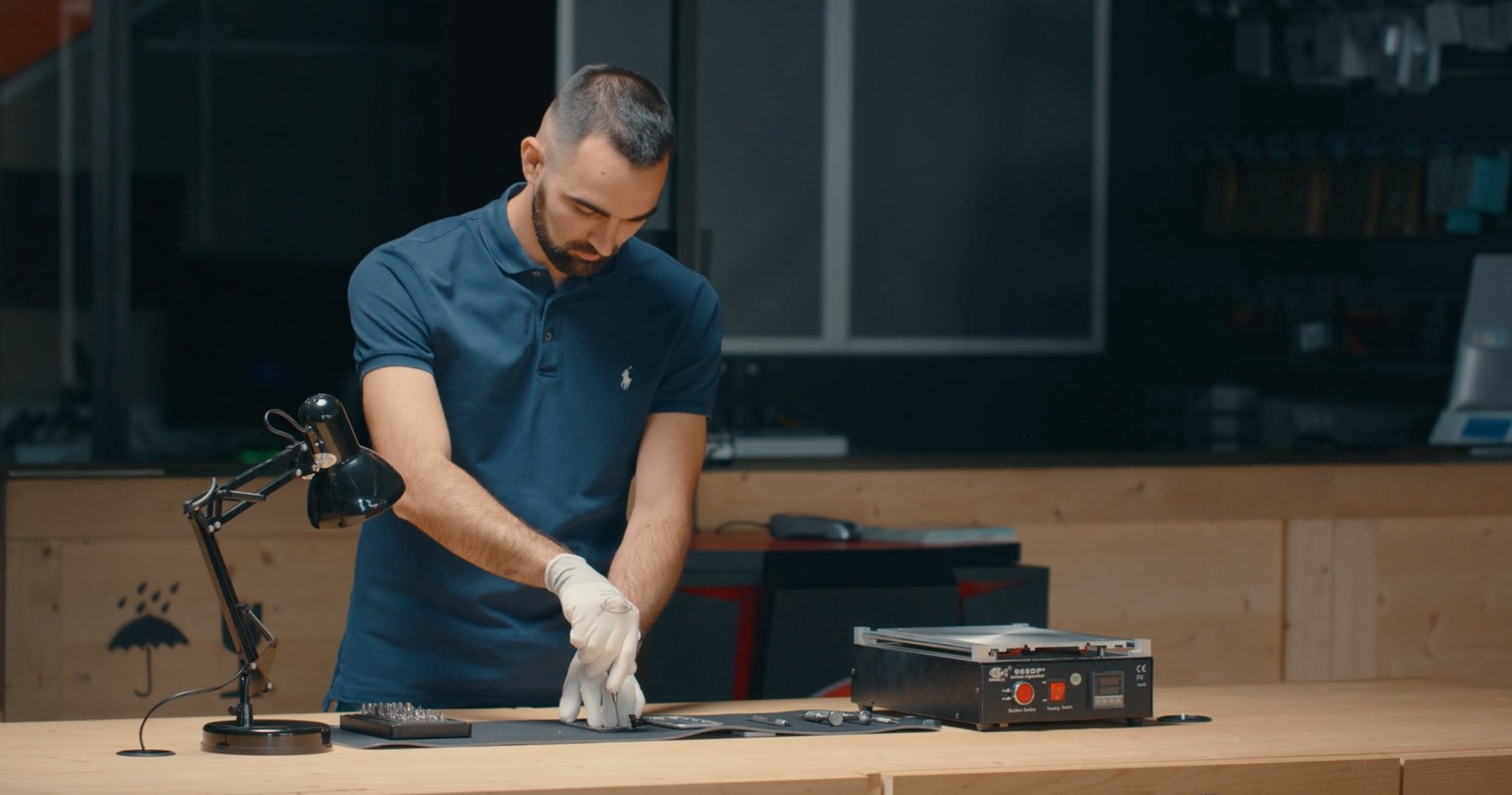 Homme en polo bleu marine qui répare un appareil électronique à un établi en bois, dans un atelier